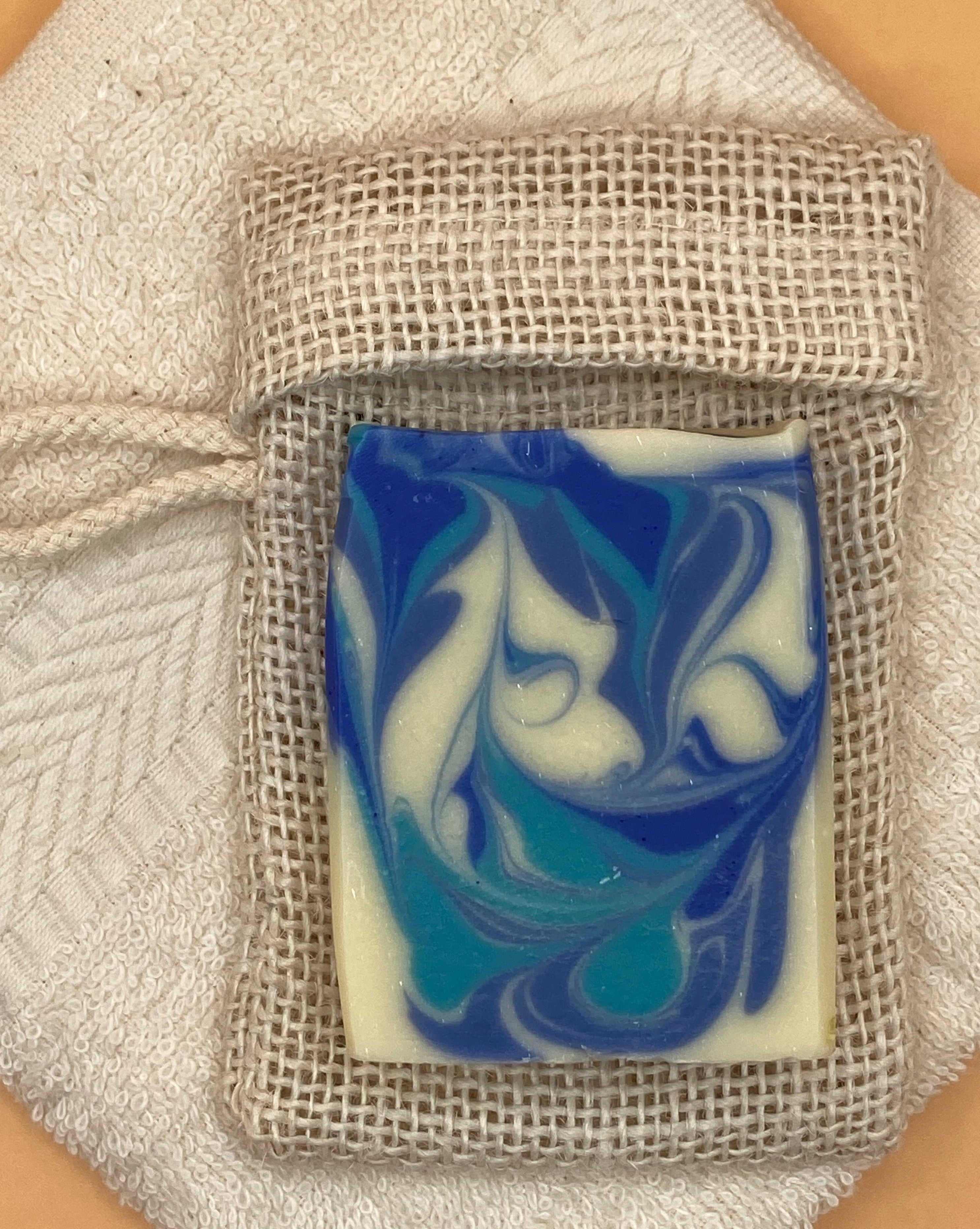Hand and body soap "Gone to the beach" soap positioned on a soap saver bag showing that the soap has the perfect fit to be inserted into the soap saver bag. 